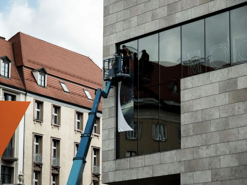 A man cleaning skyscraper windows with a harness, illustrating work on urban high-rise buildings.